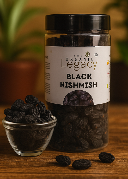 Jar of The Organic Legacy Black Kishmish on a wooden surface with a plant in the background